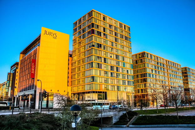 Lebendige Stadtlandschaft mit hohen Gebäuden, Straßenlaternen, Lichtern, Verkehrsampeln, Fahrzeugen, Grünflächen und einem klaren blauen Himmel im Jurys Inn Birmingham City Centre.