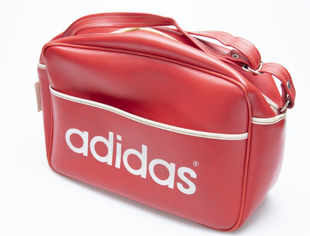 Eine rote Adidas-Sporttasche mit dem Adidas-Logo auf der Vorderseite, zwei Griffen und mehreren Taschen, vor einem weißen Hintergrund.