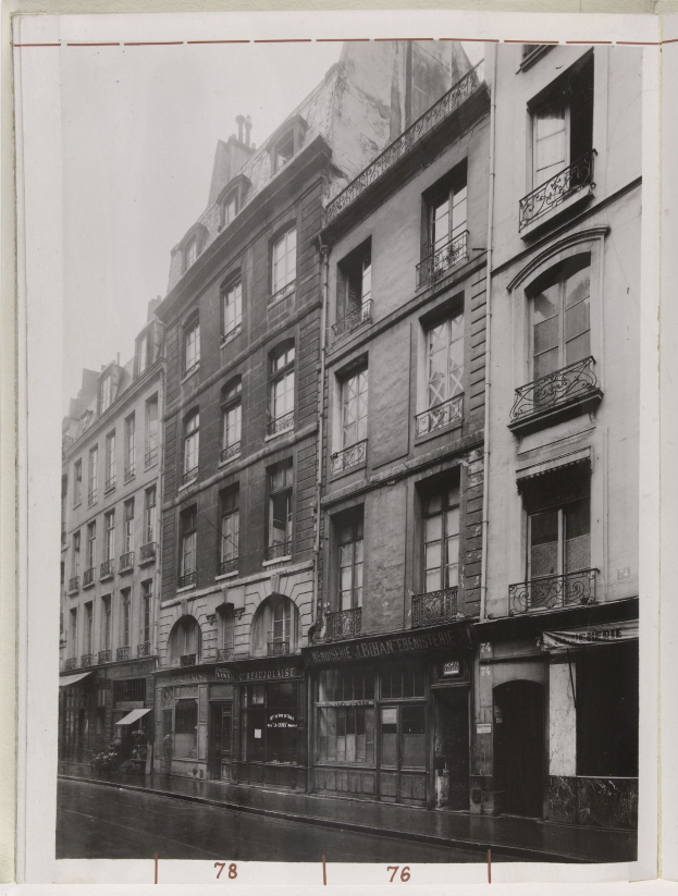 Schwarzes und weißes Foto einer Stadtstraße mit Gebäuden, Fenstern, Geländern, Namensschildern und einer Straße unten.