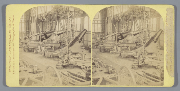 Schwarzes und weißes Foto eines alten Fabrikinneren mit einem gro├čen Geschütz in der Mitte, umgeben von kleineren Geschützen und Metallstangen auf dem Boden, und lesbarem Text auf der linken Seite.