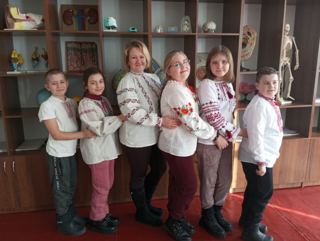 Eine Gruppe von Kindern in traditioneller ukrainischer Kleidung vor einem Regal mit Spielzeug, einem Skelett und anderen Gegenständen.