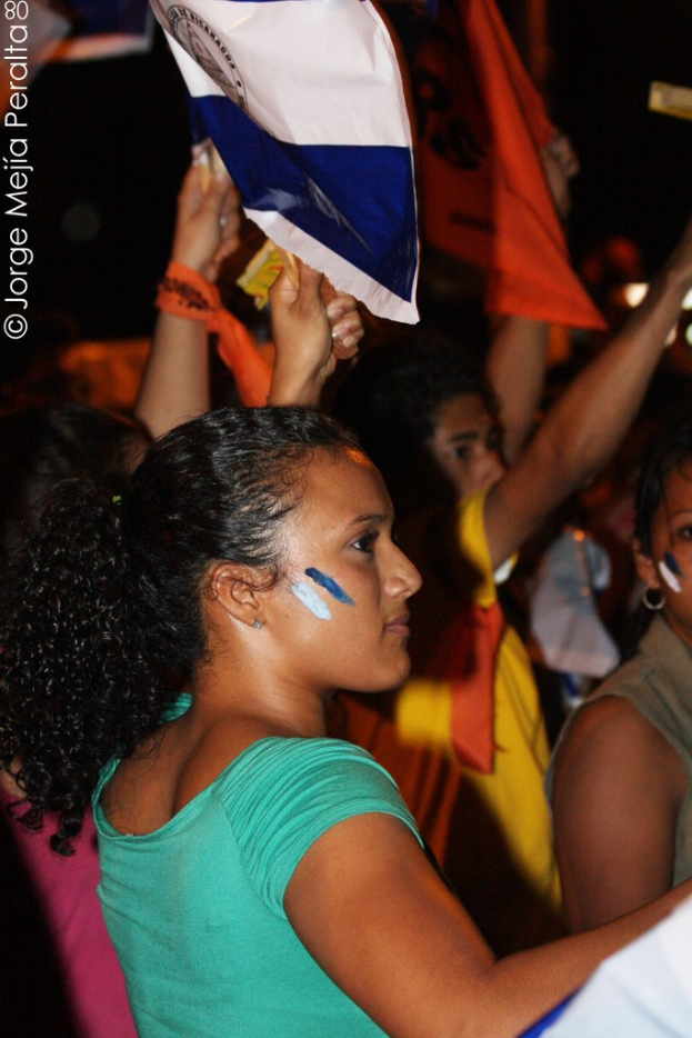 Frauen in grünen T-Shirts halten weiße Decke während einer Demonstration, mit mehreren Mädchen dahinter.