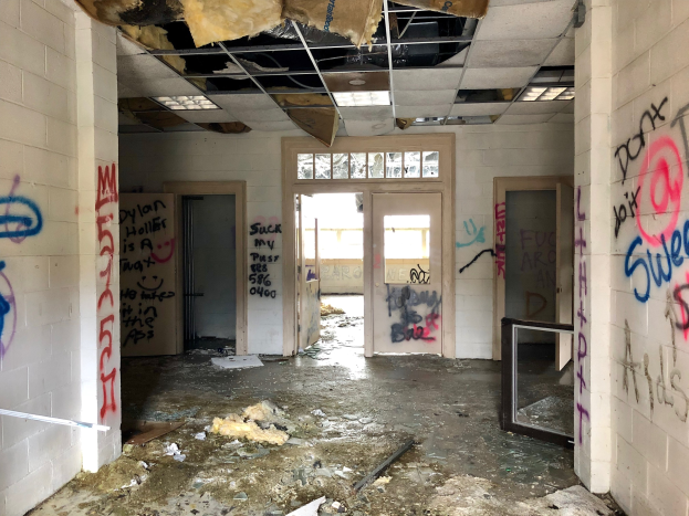 Verlassener Gebäuderaum mit Graffiti-bedeckten Wänden und Decke, Schutt auf dem Boden, mehreren Türen und Fenstern im Hintergrund und verstreuten Gegenständen.