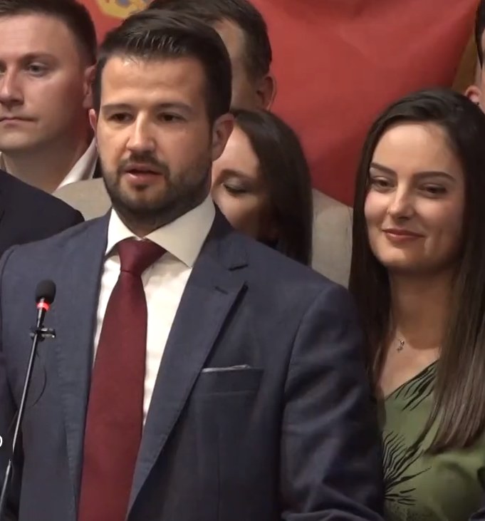 Ein Mann im Anzug spricht an einem Podium mit einem Mikrofon zu einer Menge hinter einem Banner, wahrscheinlich über ein Regierungsverbot von sozialen Medien.