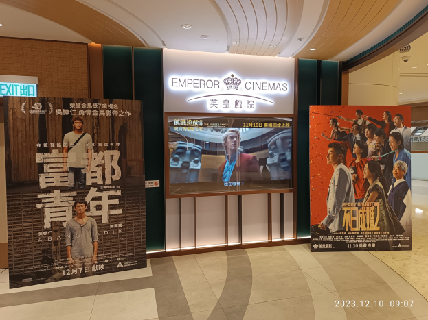 Eintritt zu den Kaiserkinos in Hong Kong mit Bannern, einem Bildschirm, einer Namensplakette, Deckenleuchten und einem Wasserzeichen.