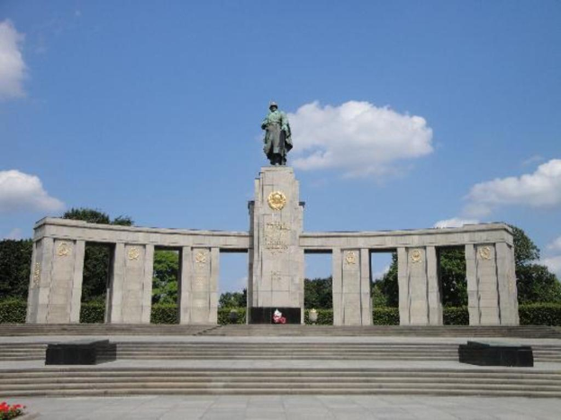 Ein Denkmal mit Säulen und einer Statue darauf, umgeben von Bäumen und einem bewölkten Himmel, mit Stufen, die hinaufführen.
