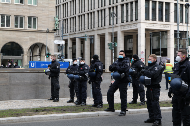 Polizisten in schwarzen Uniformen und Masken stehen vor einem Berliner Gebäude mit Glasfenstern und Säulen, einige halten Helme.