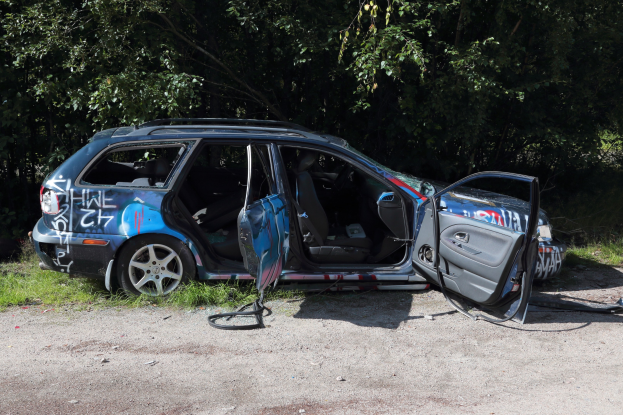 Ein Auto nach einem Crash am Straßenrand, mit Gras und Bäumen im Hintergrund.