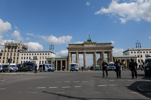 Eine Gruppe von Polizisten vor dem Brandenburger Tor in Berlin, Deutschland, mit den Säulen und der Statue des Tors im Vordergrund, umgeben von Gebäuden und Fahrzeugen auf der Straße.