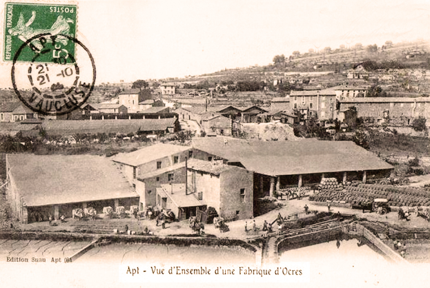 Ein altes Schwarz-Weiß-Foto einer Stadt mit einem Stempel, das Gebäude, Bäume und Menschen zeigt, mit Text unten.