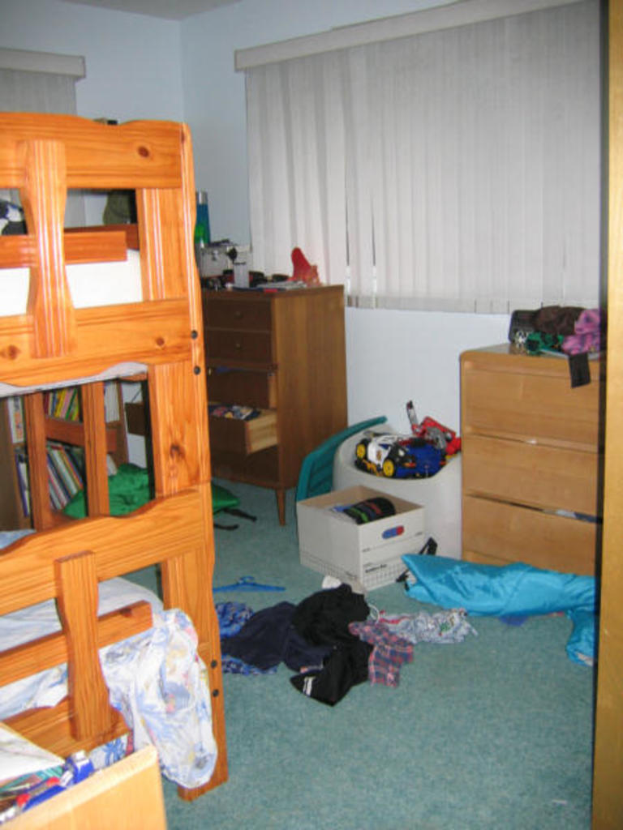 Ein Raum mit einem Stockbett, einem Schreibtisch, einem Tisch und diversen Gegenständen auf dem Boden.