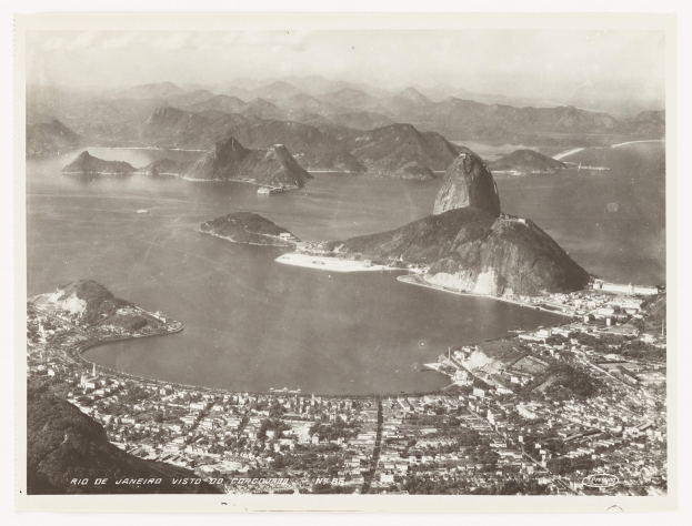 Schwarzer und weißer Luftaufnahme von Rio de Janeiro, Brasilien, mit dem Zuckerhut im Hintergrund, sichtbarem Wasser, Hügeln und Stadtgebäuden darunter.