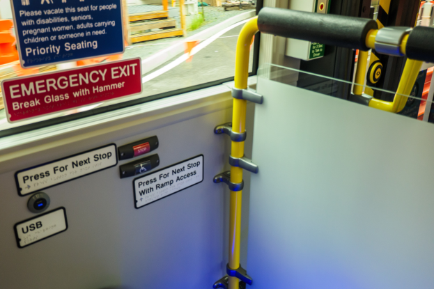 Notausgangsschild an der Seite eines Zuges mit einer Tür, Griff und Glasfenster, das Straße, Pfosten und Outdoor-Objekte zeigt.