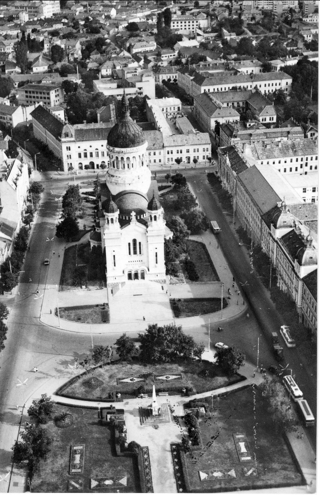 Eine Luftaufnahme einer Stadt mit einer zentralen Kirche, umgeben von Gebäuden, Bäumen, Straßen, Fahrzeugen, Polen und Menschen, mit Text unten.