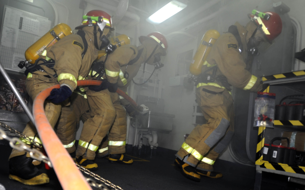 Feuerwehrleute in Schutzausrüstung mit Sauerstoffflaschen arbeiten in der Nähe eines Feuerwehrautos.