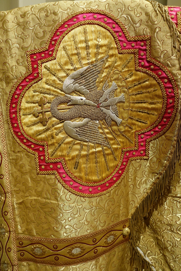Nahaufnahme eines Priestergewandes mit goldenen und roten Stickereien vor einer Wand im Hintergrund.