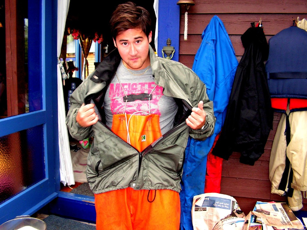 Eine Jacke und ein T-Shirt sind im Zentrum des Bildes, mit verschiedenen Artikeln wie Jacken, Zeitungen, einem Haus mit Vorhängen, einer Tür, Fenstern, einer Glocke und einer Wand im Hintergrund.