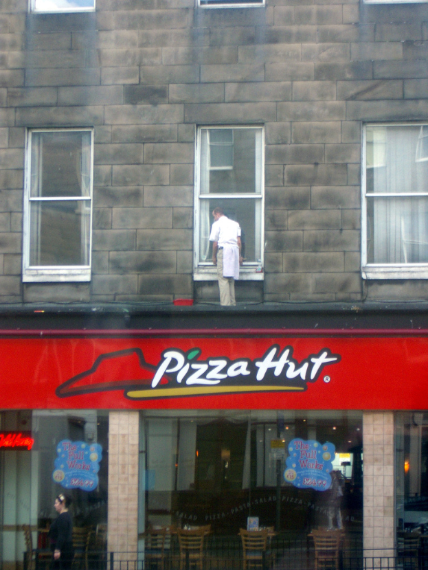 Ein Pizza Hut-Laden mit einem Mann, der die Glasscheiben oben reinigt und ein rotes Schild davor.