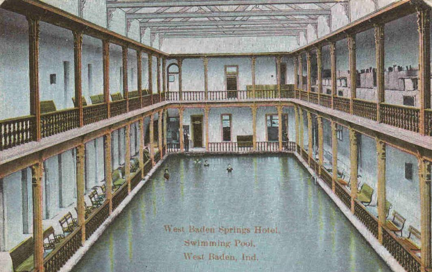 Eine alte Postkarte, die ein Hallenbad im West Baden Springs Hotel zeigt, mit Menschen, die schwimmen, und verschiedenen architektonischen Elementen drumherum, sowie Text unten.