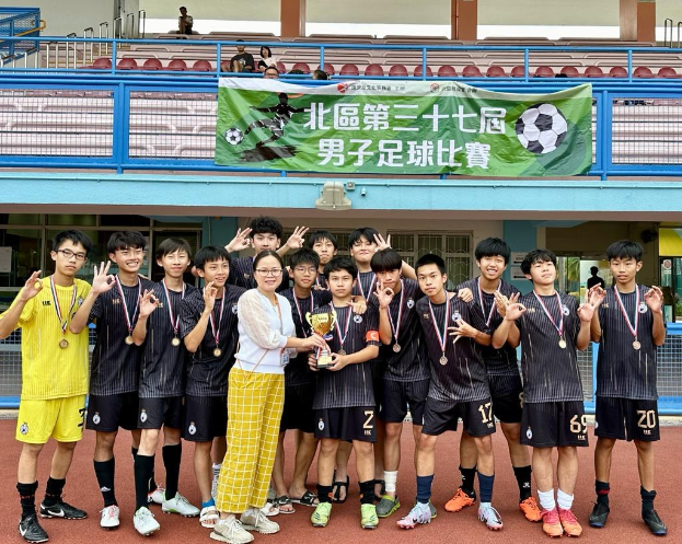 Gruppe junger Männer in Fußballtrikots auf einem Feld stehend, Medaillen tragend und einen Pokal haltend, mit einem Banner im Hintergrund, das 'Yokohama U-16 Jungenfußballteam' lautet.