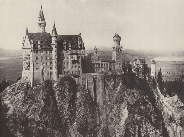 Neuschwanstein Burg in Deutschland, thront auf einem Berg umgeben von Bäumen und einem klaren Himmel, dargestellt in Schwarz-Weiß.