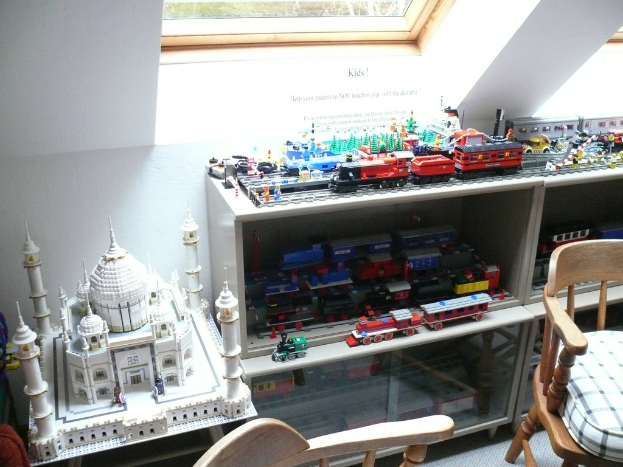 Ein Glasfenster oben in der Mitte, ein Stuhl rechts, eine Vitrine mit aufgereihten Spielzeughasen und ein Spielzeug-Taj Mahal auf einem Schreibtisch links.
