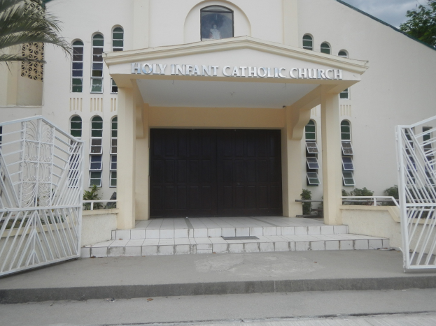 Die Heilige Infant Catholic Church mit Treppen, Geländern, umgebenden Pflanzen und einem bewölkten Himmel.