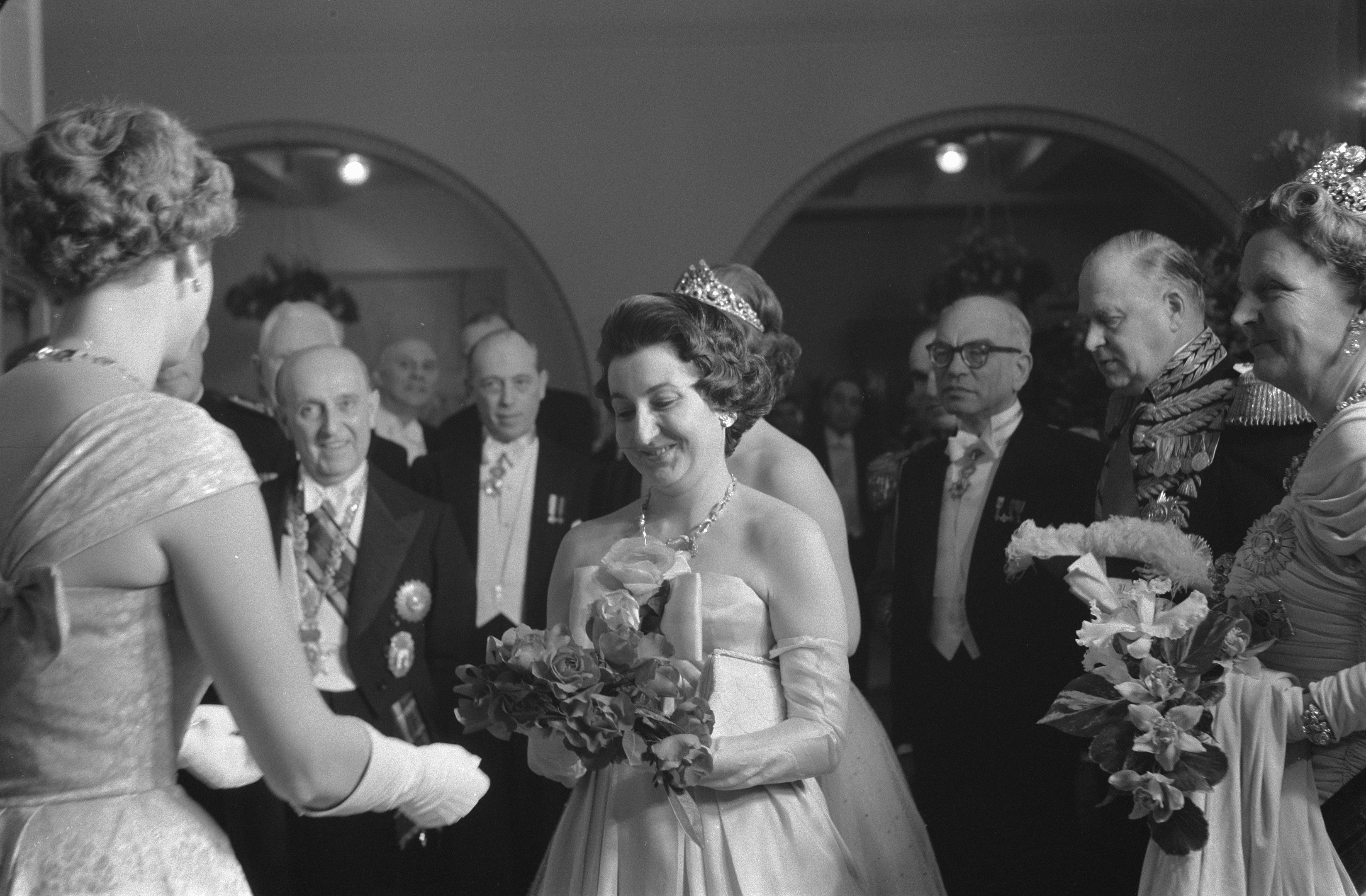 Schwarzes und weißes Foto von Queen Elizabeth II. und Prinz Philip, Duke of Edinburgh, an ihrem Hochzeitstag, die Kronen tragend und Blumensträuße haltend, umgeben von einer Gruppe von Menschen.