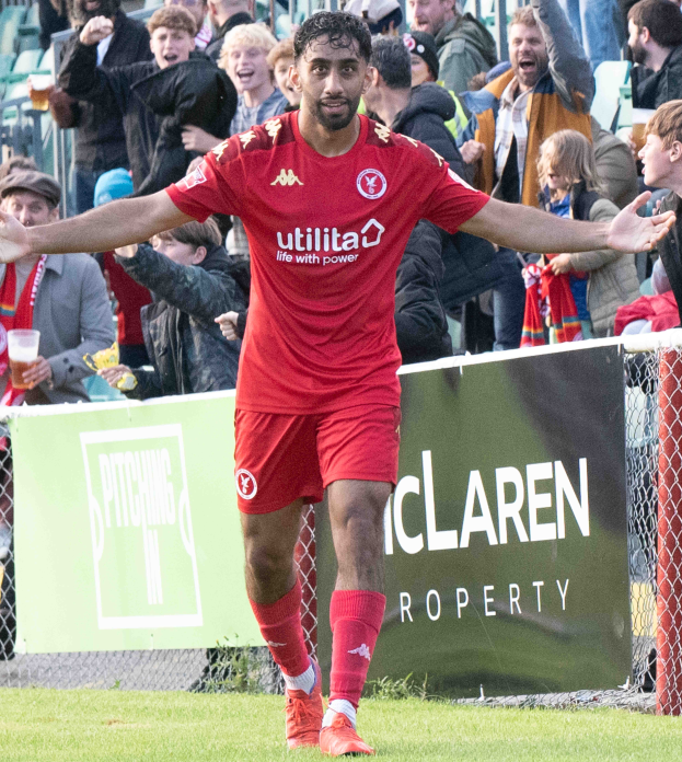 Ein Füßballer in roter Uniform rennt mit ausgebreiteten Armen auf einem Feld, im Hintergrund ist eine Menge und ein Banner mit der Aufschrift "Middlesbrough FC gegen Swansea City - Sky Bet Championship" zu sehen.