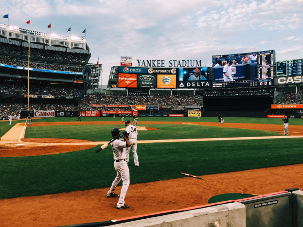 Baseballspiel im Yankee Stadium mit Spielern auf dem Feld und Zuschauern in den Rängen unter einem bewölktem Himmel.