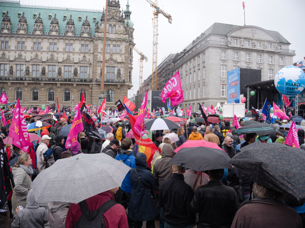Eine große Gruppe von Menschen mit Schirmen und Transparenten nimmt an einer Women's March in Berlin teil, mit Ballons und Stangen im Vordergrund und dem Himmel im Hintergrund.