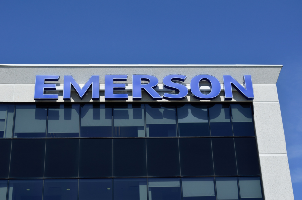 Das Emerson-Logo an der Seite eines Gebäudes mit dem Text "Emerson investiert 1,5 Milliarden USD in den USA" vor einem klaren blauen Himmel.