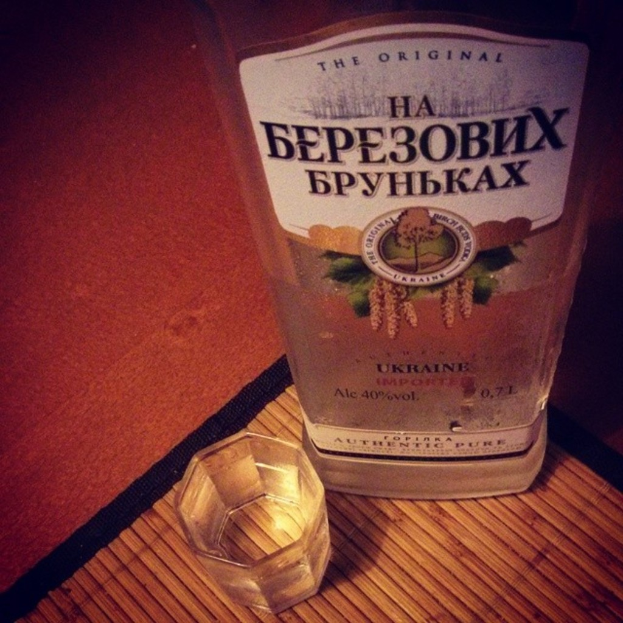 Ein klares Glas mit einer goldbraunen Flüssigkeit, das auf einer dunklen, strukturierten Unterlage steht.