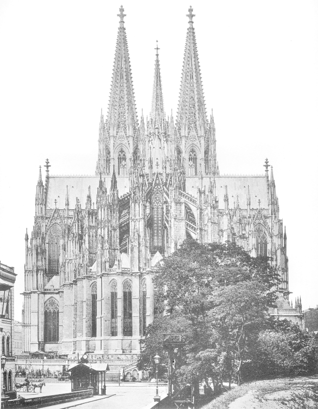 Ein Schwarz-Weiß-Foto des Kölner Doms in Köln, Deutschland, ein majestätisches Gebäude mit hohen Türmen und detaillierten Verzierungen, umgeben von Bäumen, Straßenlaternen, Straßenlaternen und Menschen auf der Straße, mit dem Himmel im Hintergrund.