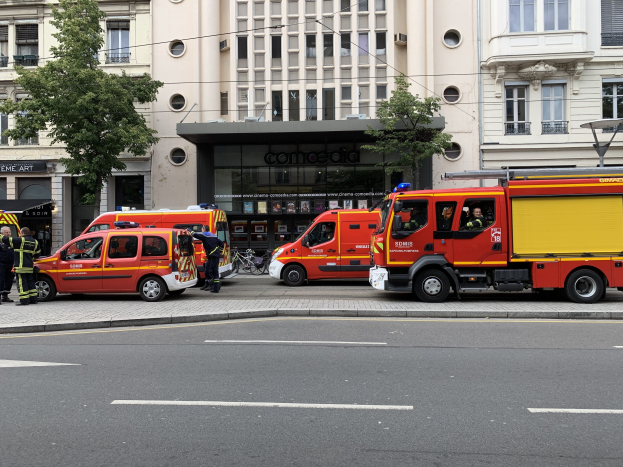 Feuerwehrfahrzeuge auf einer Straße in Paris geparkt mit Menschen in der Nähe, Gebäuden, Bäumen und einem Fahrrad im Hintergrund, wahrscheinlich am Unfallort.