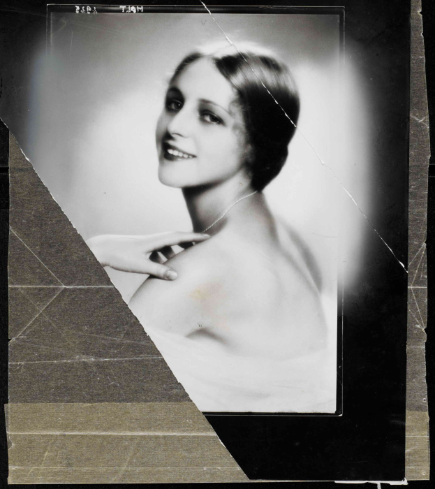 Schwarz-weißes Foto einer Frau in einem Kleid mit einer 1920er-Jahre-Frisur, die direkt in die Kamera lächelt.