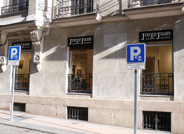 Ein mehrstöckiges Gebäude mit Fenstern, Geländern, Türen und Säulen, das Schilder an Pfosten entlang des Gehwegs und einsehbare Innenobjekte zeigt, die auf eine belebte städtische Umgebung hinweisen.