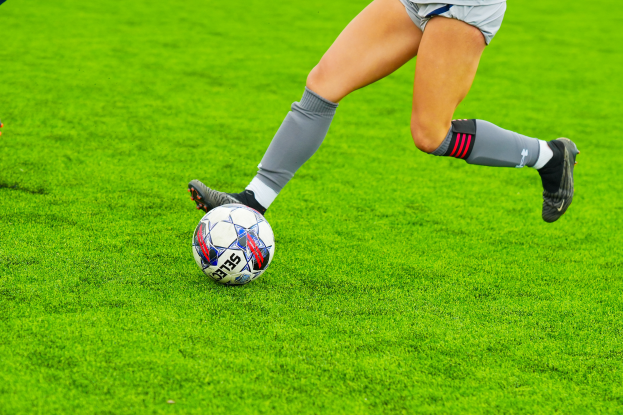 Eine Frau in Sportkleidung und -schuhen kickt einen Fußball auf einem saftig grünen Feld.