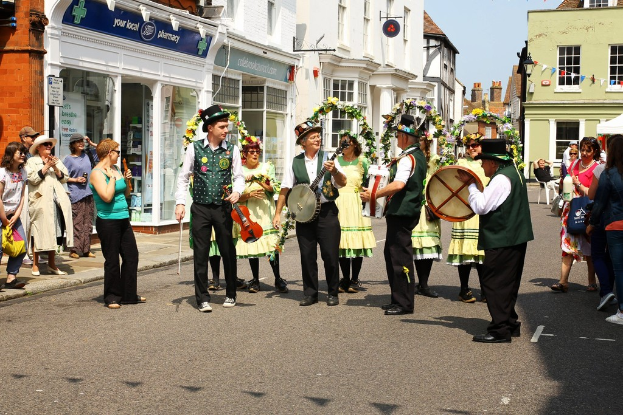 Eine Gruppe von Musikern, die Instrumente auf der Straße spielen, mit einer kleinen Menge drumherum und Geschäften mit Schildern im Hintergrund.
