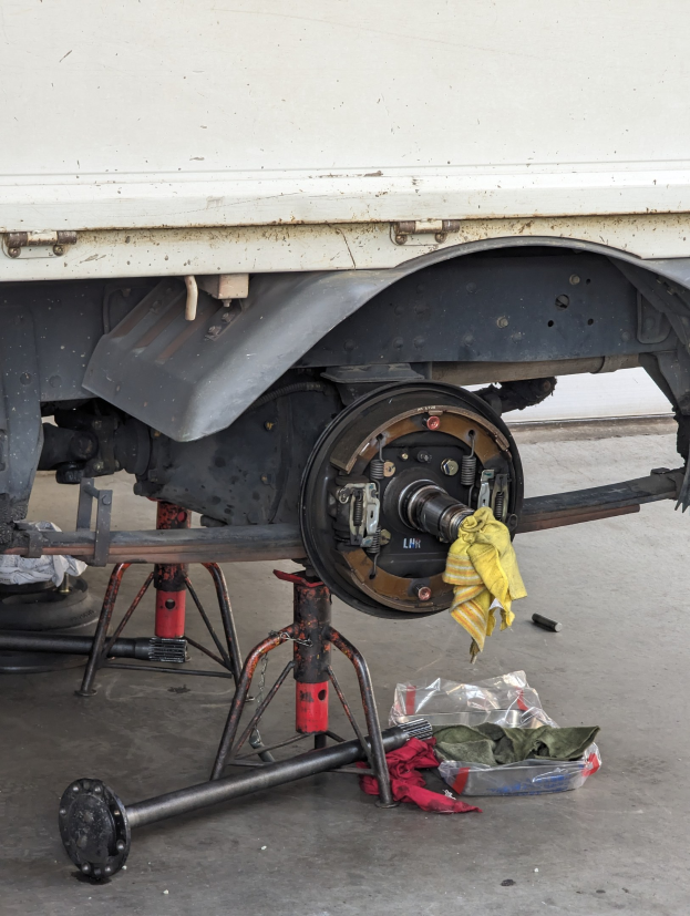 Ein gelber, mit einem Tuch bedeckter Lkw steht in einer Garage, umgeben von Werkzeugen und Gegenständen auf dem Boden.