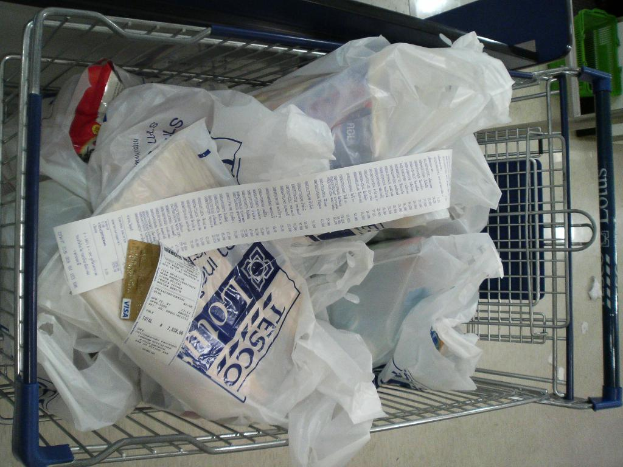 Ein Einkaufswagen voller Plastikverpackungen und eine Rechnung, mit einem grünen Korb oben rechts.
