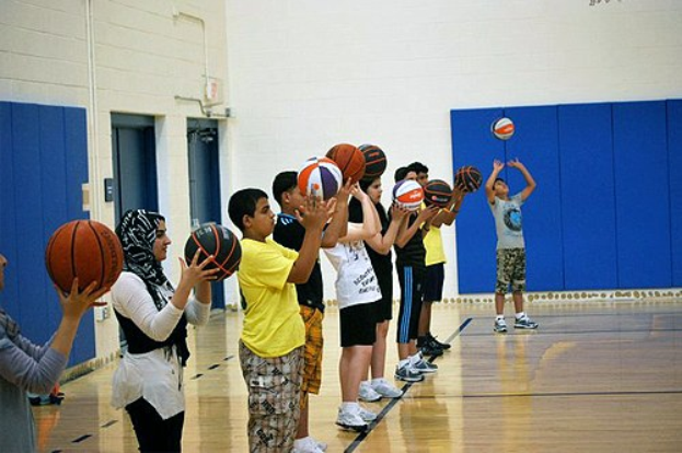 Gruppe junger Menschen auf einem Basketballfeld mit Basketballs, Türen und einer Wand im Hintergrund.