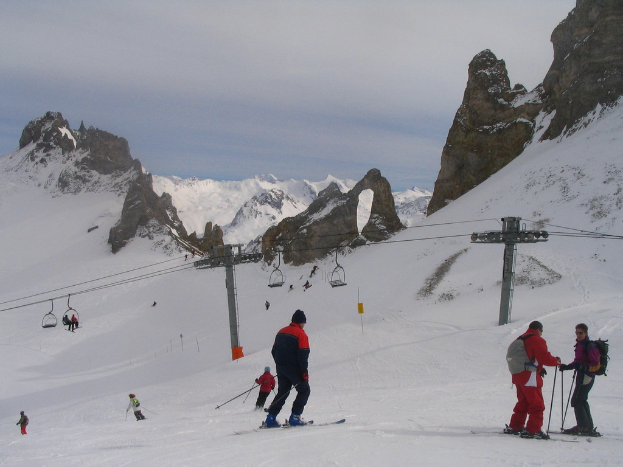 Menschen in Pullis skifahren auf Eis mit einem Seilbahn, Bergen und einem bew├Âlktem Himmel im Hintergrund.