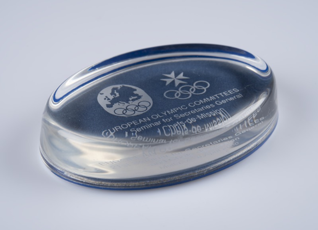 Ein klarer Glasteller mit einem blauen und weißen "Europäischer Olympische Ausschuss"-Logo auf einer weißen Oberfläche.