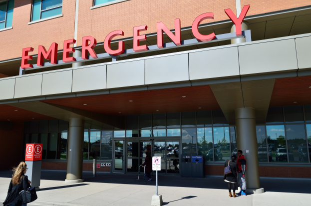 Gruppe von Menschen, die vor einem Notaufnahmeschalter mit Glaswänden, Säulen und Schildern gehen