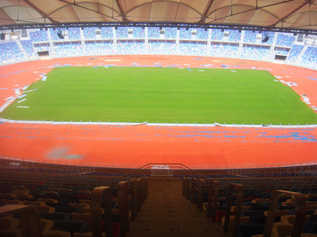 Großes Stadion mit vielen Zuschauern, Featurend dreigeschossige Sitzreihen, Geländer, Treppen und ein Dach, mit dem Spielfeld in der Mitte sichtbar.