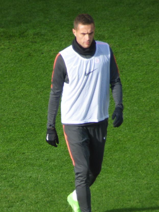 Ein Mann in einem weißen Hemd, schwarzen Hosen und grünen Schuhen läuft über ein saftiges grünes Feld.