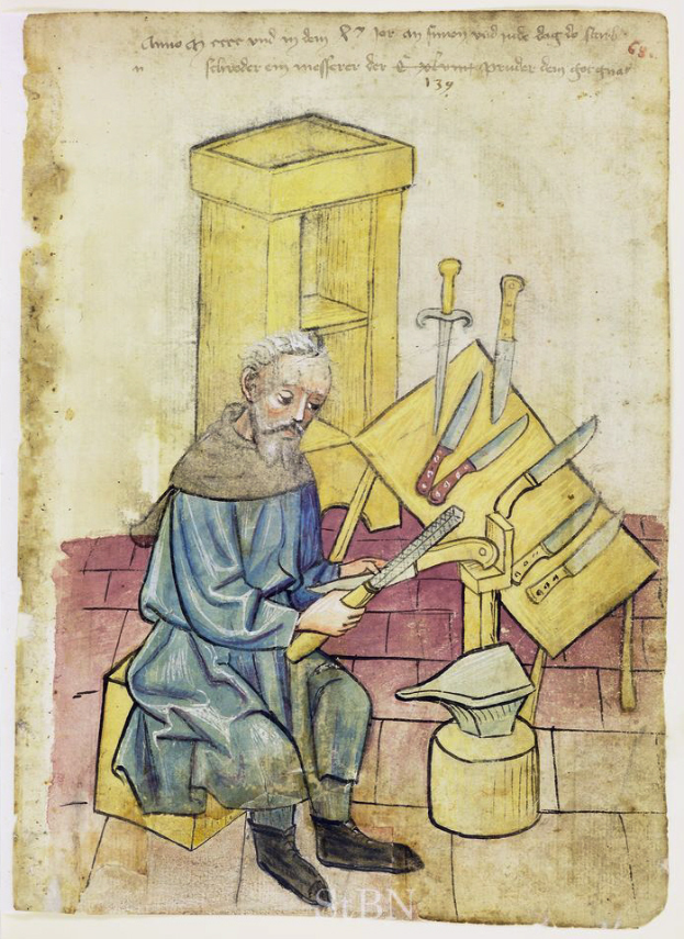 Ein älterer Mann sitzt auf einem Stuhl, hält in einer Hand ein Messer und in der anderen ein Stück Papier mit Schrift darauf, mit mehreren Messern auf dem Tisch vor ihm.