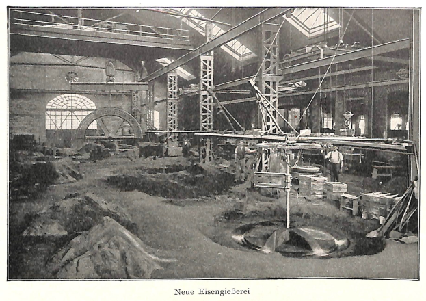Schwarzes und weißes Foto eines Fabrikinneren mit Arbeitern, die Maschinen bedienen, Metallstangen und -stöcke; Text unten lautet 'Neue Eisenglebeerei, die erste Fabrik in Deutschland'.