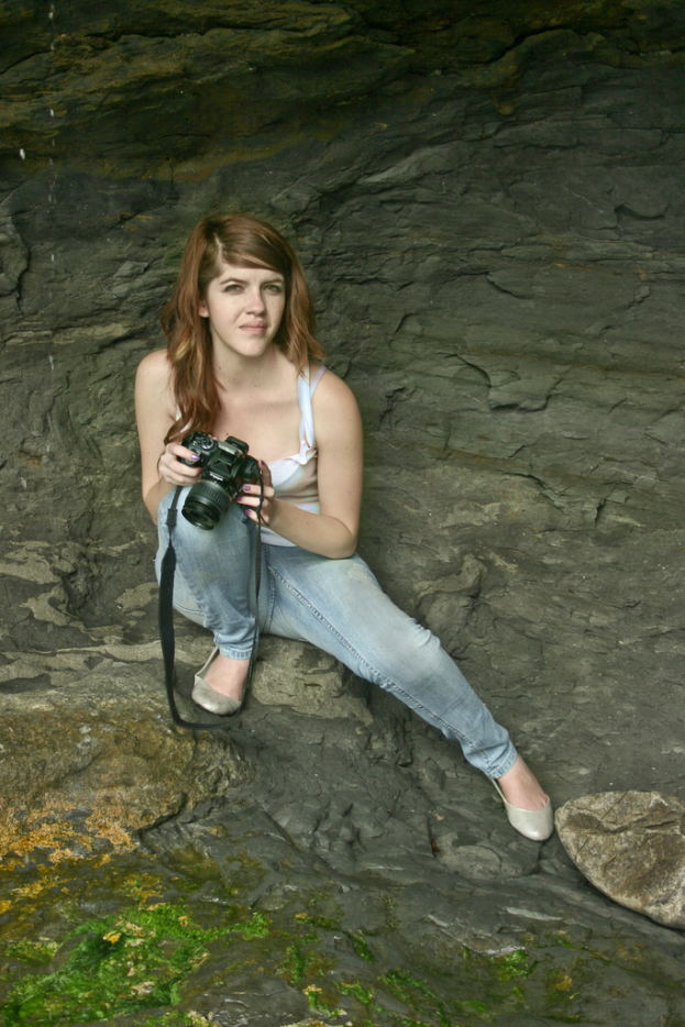 Eine Frau mit einer Kamera vor einem Felsen im Hintergrund.